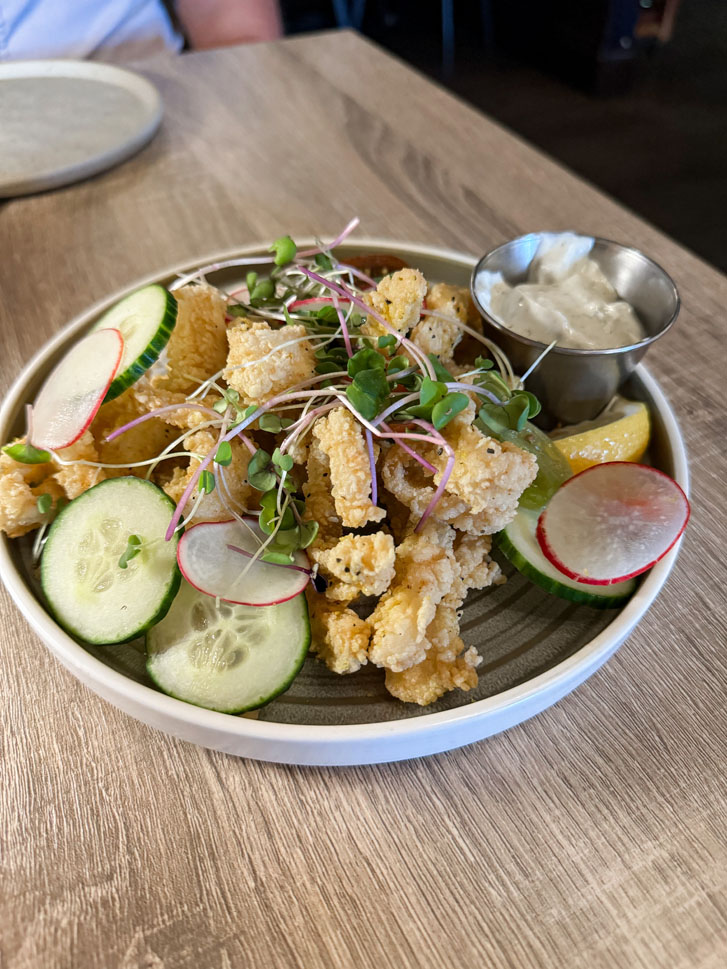 a plate of fried fish, cucumber slices and a sauce