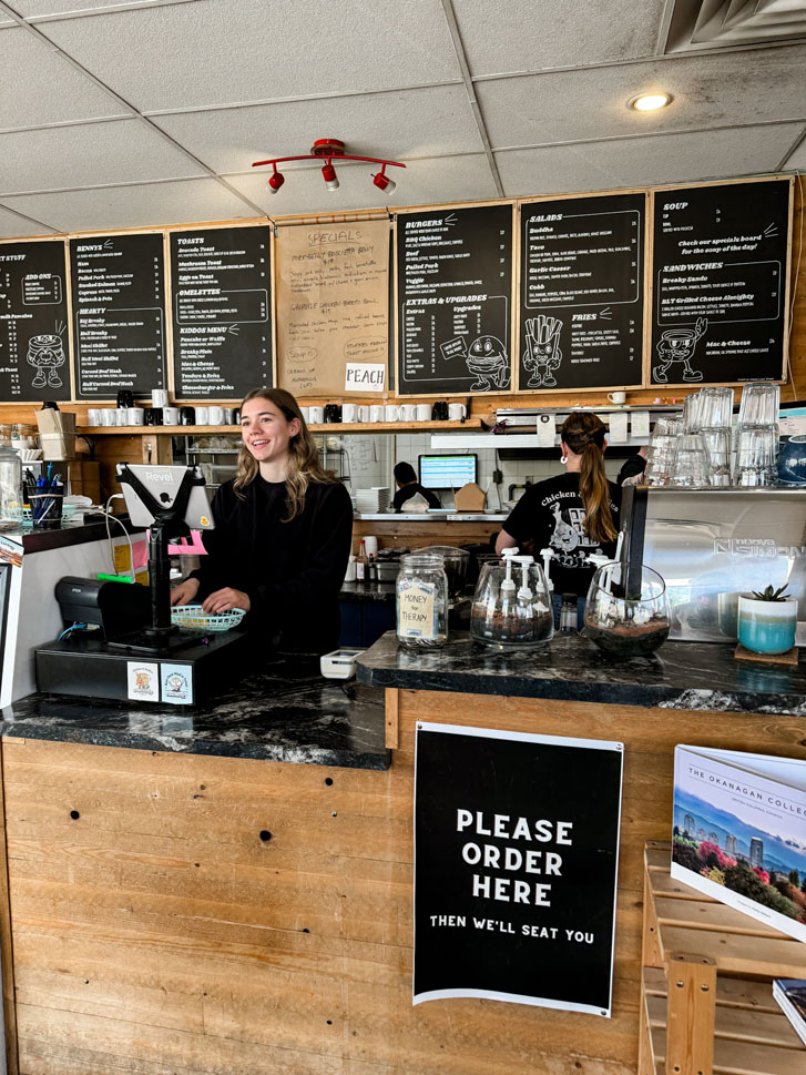 a restaurant counter with a lady behind it and chalkboard menus hanging on the walls behind her