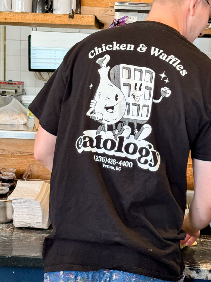 Man wearing a black shirt that reads 'chicken & waffles' and 'Eatology'