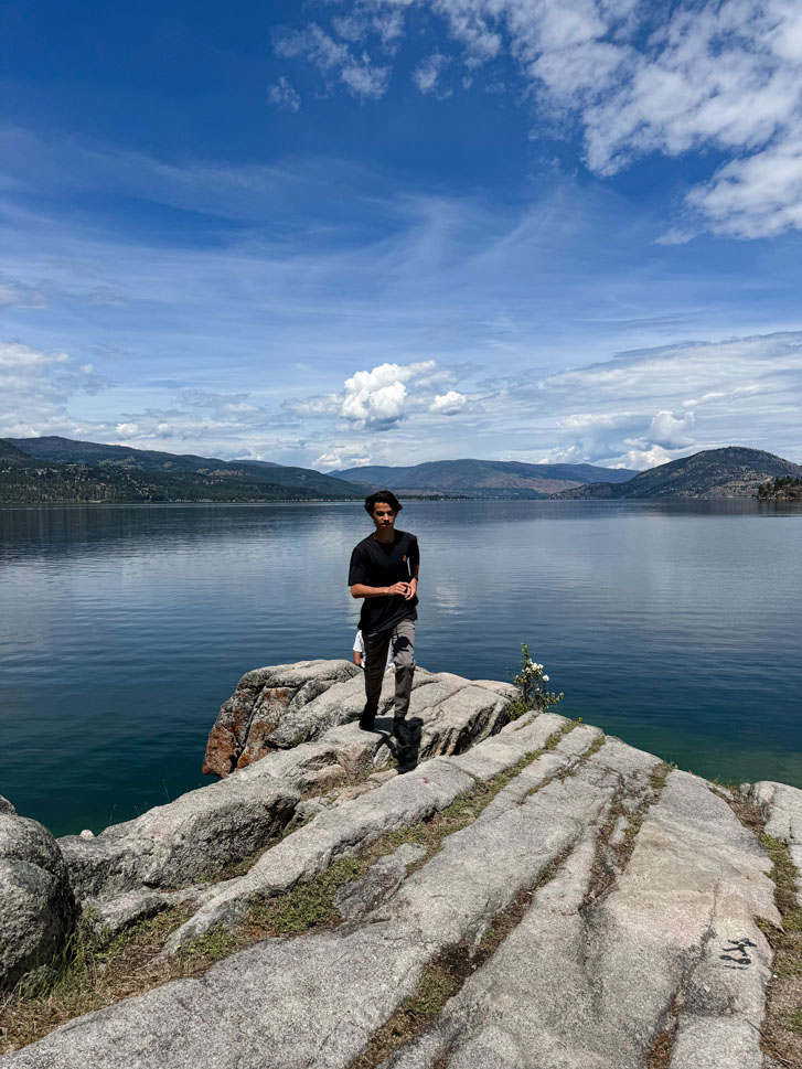 a boy walking on a rock beside a huge lake with the skies in view