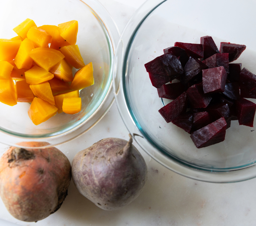 cubed golden beets in a bowl next to a bowl of cubed red beets, with two whole beets on a white countertop