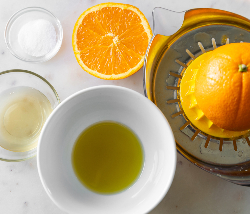 orange, olive oil, salt, and other ingredients for a salad dressing on a white counter 