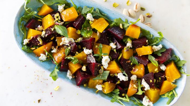 yellow and red beet salad with goat cheese, pistachios and arugula in a blue serving dish