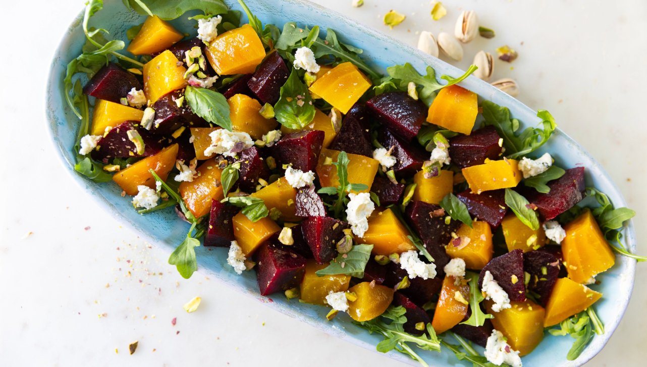 yellow and red beet salad with goat cheese, pistachios and arugula in a blue serving dish