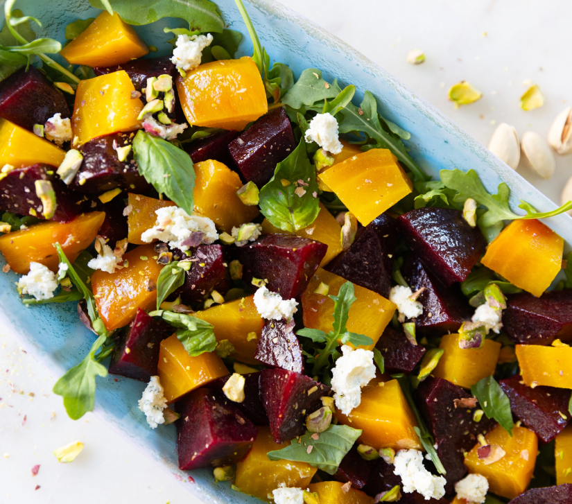 red and yellow beet salad with goat cheese and arugula in a blue serving dish