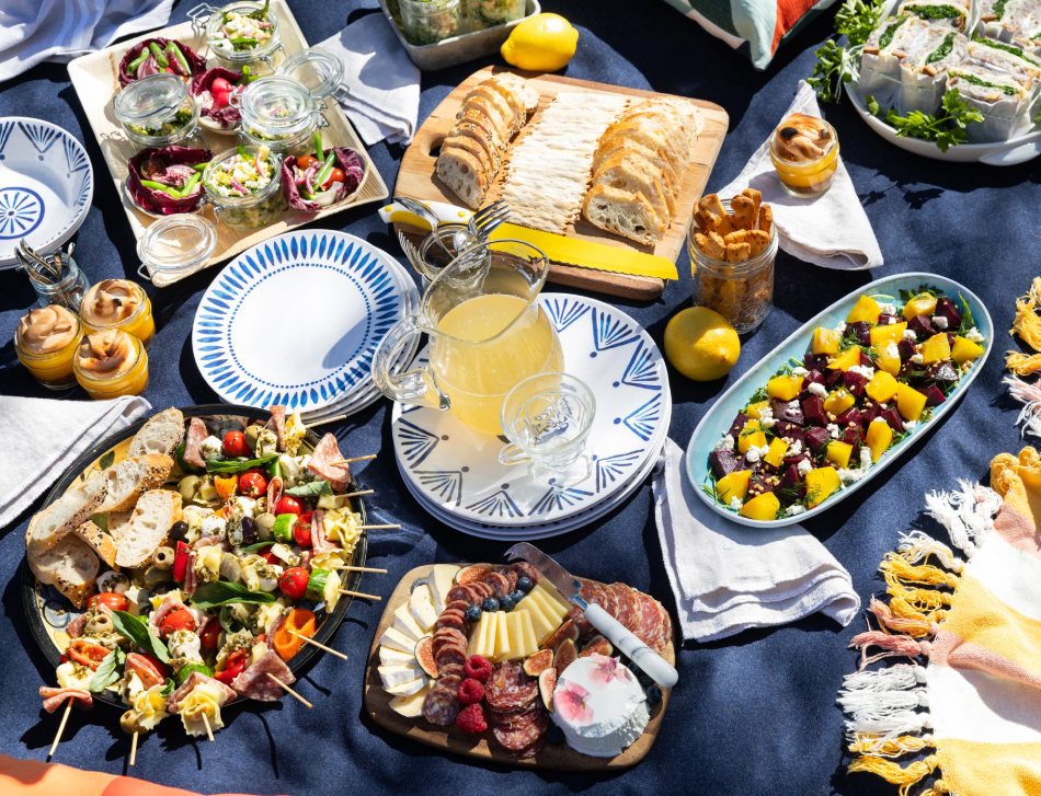 picnic on a blue blanket with an array of food and drink items and a beet salad
