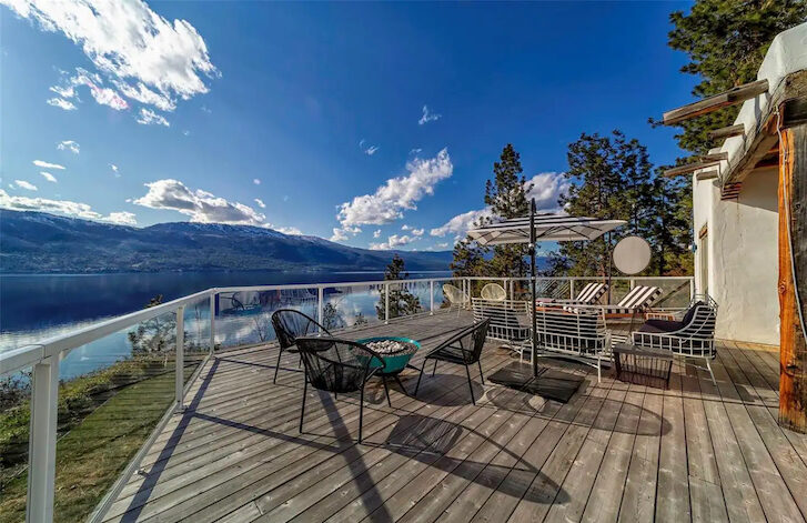 an outdoor deck with chairs and tables and a lake