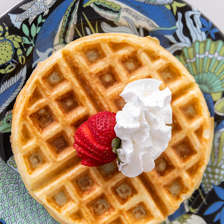 waffle with whipped cream and strawberry slices on a blue and green patterned plate