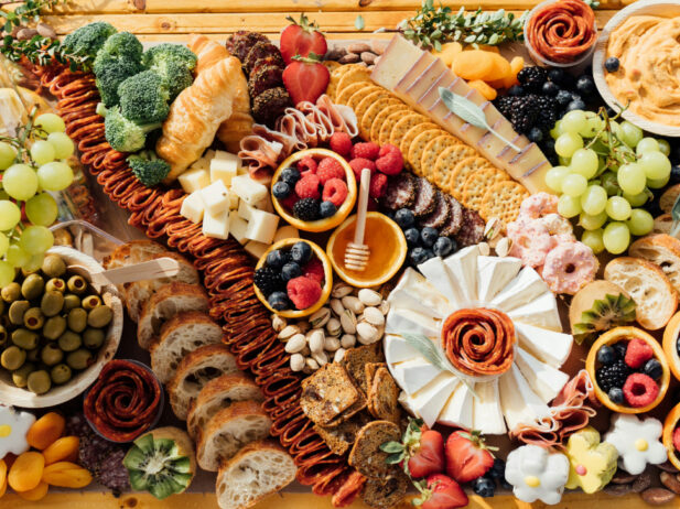 wooden table filled with charcuterie, fruit, spreads, and crackers