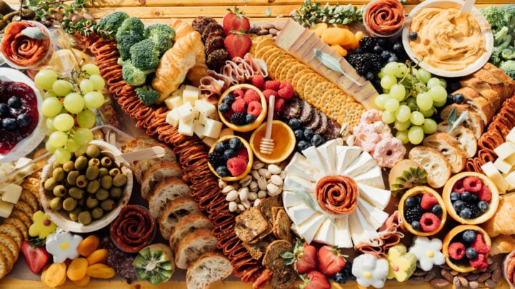 wooden table filled with charcuterie, fruit, spreads, and crackers