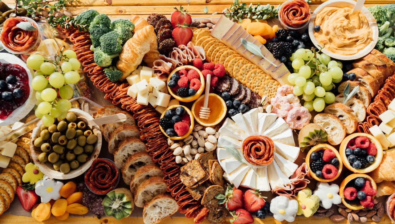 wooden table filled with charcuterie, fruit, spreads, and crackers
